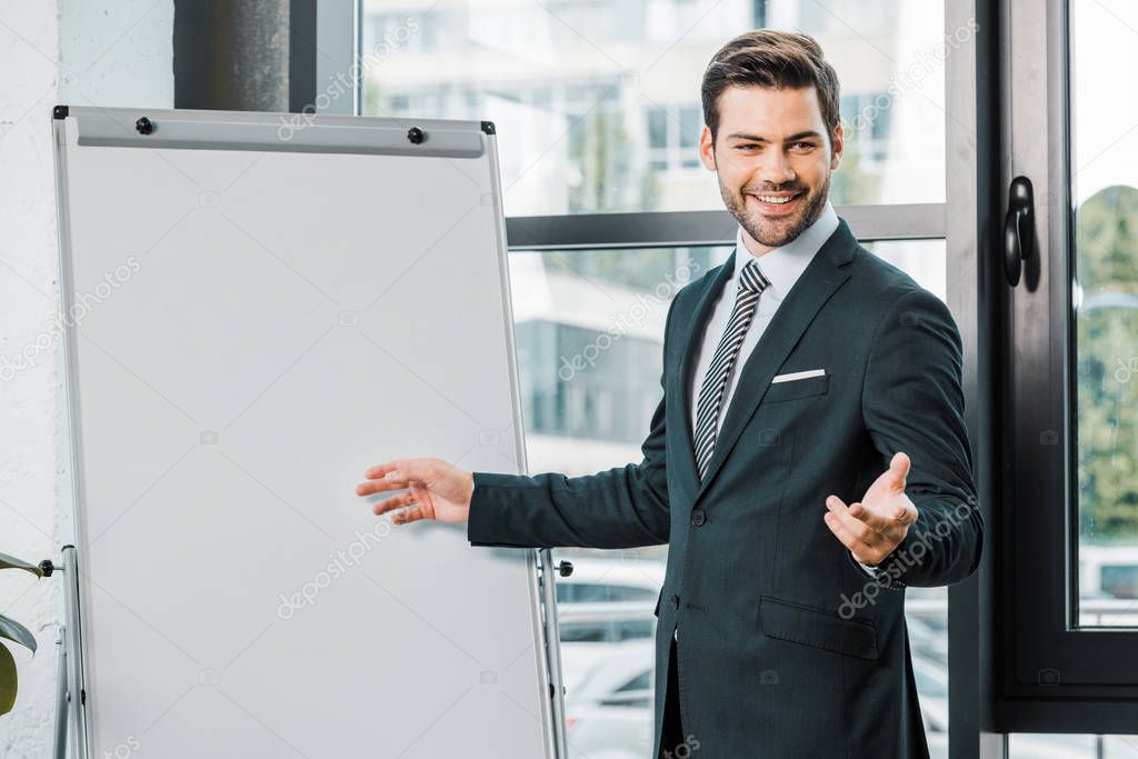 portrait of cheerful businessman in suit standing at empty white board in office