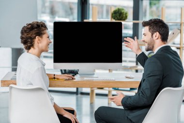 smiling business colleagues having discussion at workplace with blank computer screen in office clipart