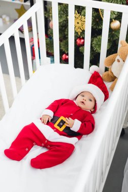 güzel küçük bebek Santa görünümünü yüksek açı uygun oyuncak ayı ile beşik içinde yatan ve kameraya bakıyor