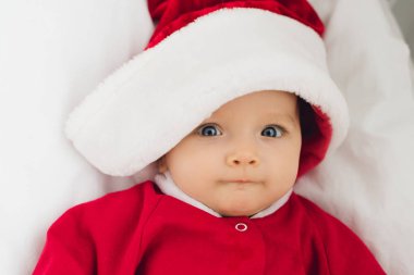 yakın çekim küçük bebek yatakta yatan ve kameraya bakarak Noel Baba kıyafetli portresi
