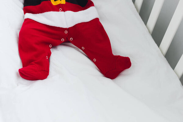 cropped shot of little baby in santa suit lying in infant bed