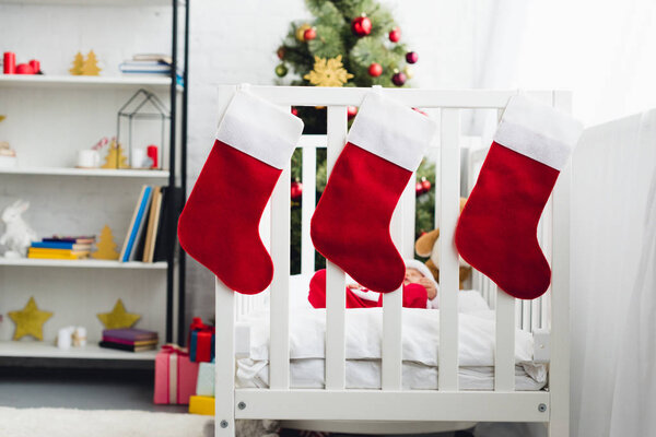 gift socks hanging on infant bed with little baby in santa suit inside