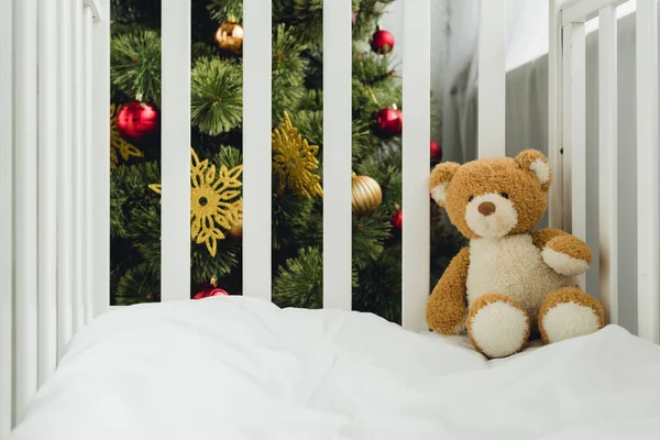 クリスマス ツリーの前で幼児のベッドにテディベア  — 無料ストックフォト