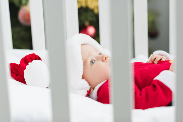 close-up shot of adorable little baby in santa suit lying in crib