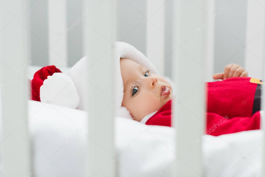 close-up shot of beautiful little baby in santa suit lying in crib