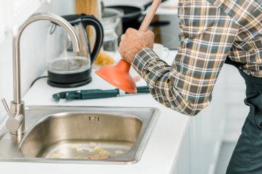 cropped image of plumber using plunger and cleaning sink in kitchen clipart