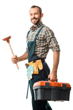 smiling handsome plumber holding plunger isolated on white and looking at camera clipart