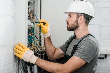 yakışıklı sakallı elektrikçi elektrik kutusu onarım ve koridorda tornavida kullanarak yan görünüm