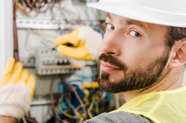 yakışıklı elektrik kutusu tamiri, koridorda tornavida kullanarak ve kameraya bakarak elektrikçi sakallı