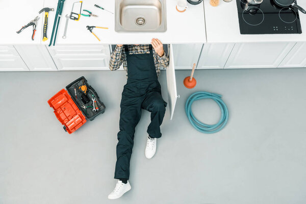 high angle view of plumber lying on floor and checking sink in kitchen
