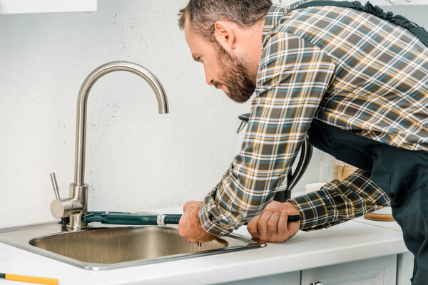 handsome plumber repairing tap with monkey wrench in kitchen