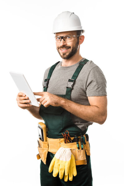 smiling handsome electrician in helmet and protective glasses using tablet isolated on white
