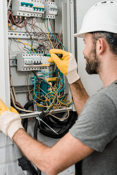 side view of electrician repairing electrical box and using screwdriver in corridor