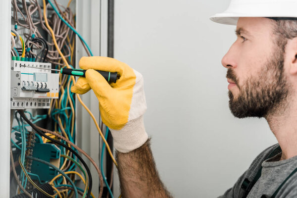 side view of handsome electrician repairing electrical box and using screwdriver in corridor