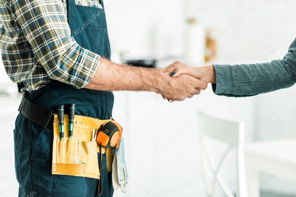 cropped image of plumber and client shaking hands in kitchen