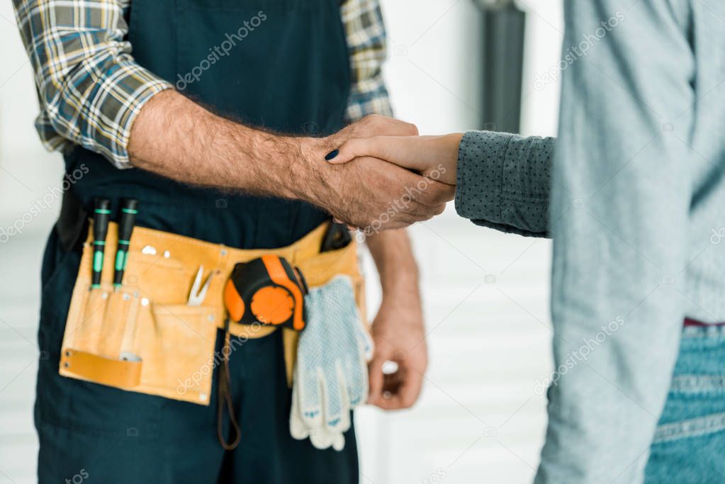 cropped image of plumber and customer shaking hands in kitchen