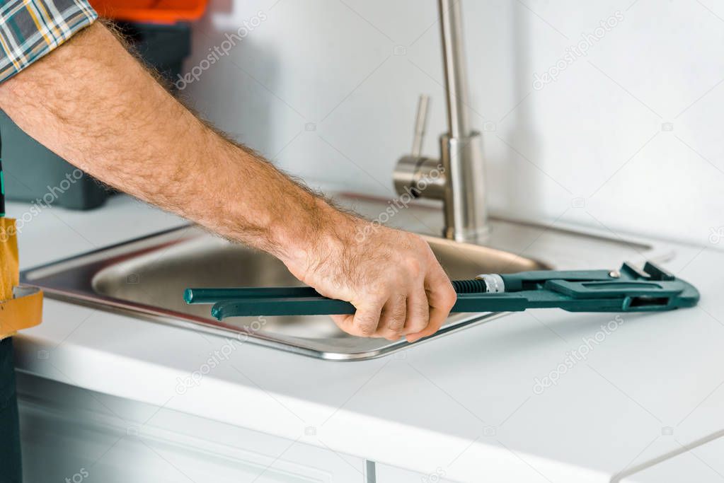 cropped image of plumber holding monkey wrench near sink in kitchen