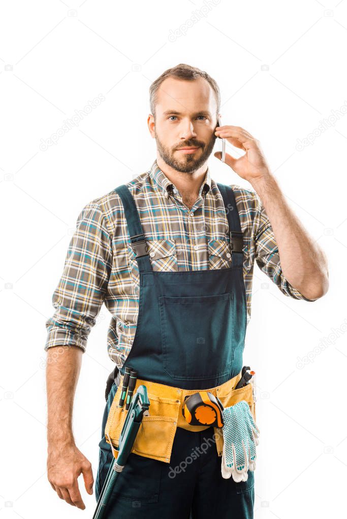 handsome plumber talking by smartphone and looking at camera isolated on white