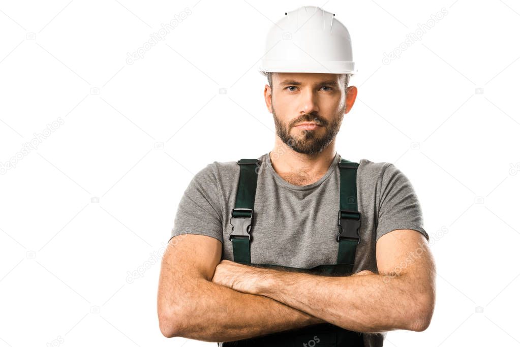 handsome plumber in helmet standing with crossed arms and looking at camera isolated on white