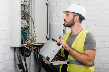 Araç kutusu tutarak ve koridorda elektrik kutusu bakarak yakışıklı elektrikçi yan görünüm