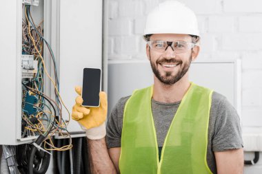 gülümseyen yakışıklı elektrikçi elektrik kutusu koridorda yakınındaki Smartphone boş ekran ile gösterilen