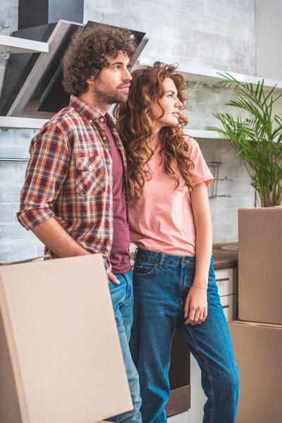 couple standing near cardboard boxes and looking away at new kitchen