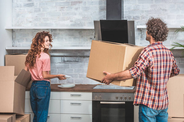 boyfriend and girlfriend with curly hair unpacking cardboard boxes together at new kitchen