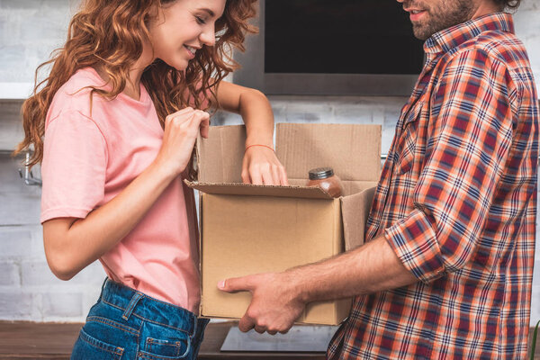 cropped image of couple unpacking cardboard box at new home