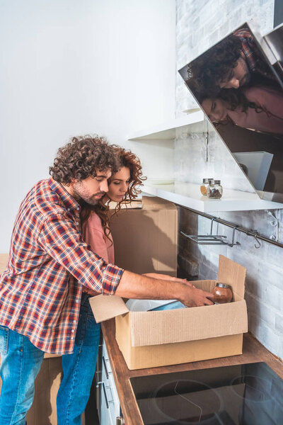 side view of couple hugging and unpacking cardboard box in new kitchen