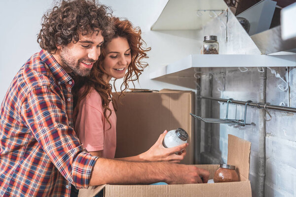 smiling couple unpacking cardboard boxes at new home, girlfriend holding salt maid