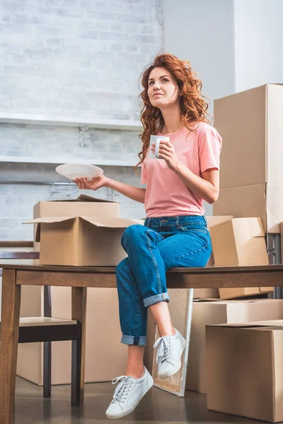 fincan kahve ve plaka, karton kutu yeni evde masada oturan tutan güzel kadın