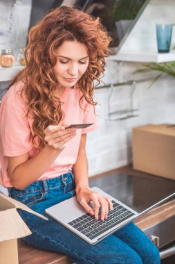 kredi kartı tutan ve yeni daire dizüstü kullanarak gülümseyen genç kadın