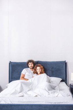 mutlu genç çift yatakta yatarken ve kameraya gülümseyen