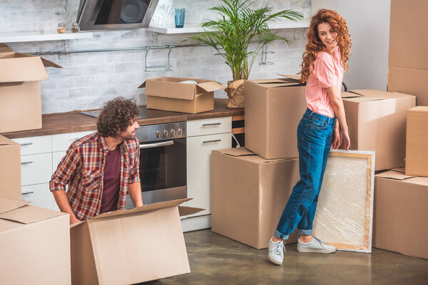 couple unpacking cardboard boxes at new home and looking at each other