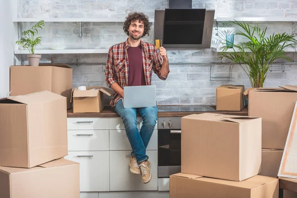 Sorrindo Bonito Homem Sentado Com Laptop Cartão Crédito Balcão Cozinha — Fotografia de Stock