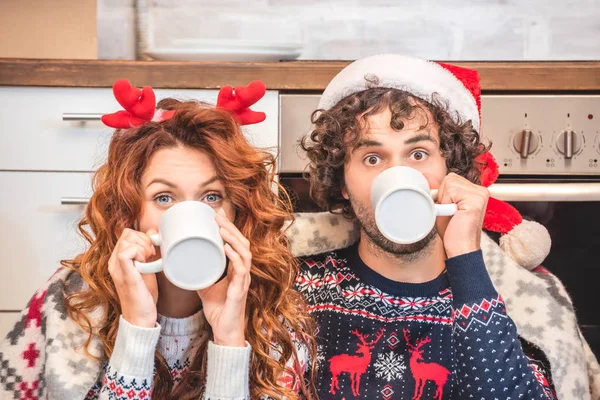 Joven Pareja Bebiendo Tazas Mirando Cámara Mientras Celebra Navidad Nuevo — Foto de Stock