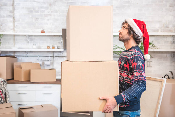 side view of young man in santa hat holding cardboard boxes during relocation