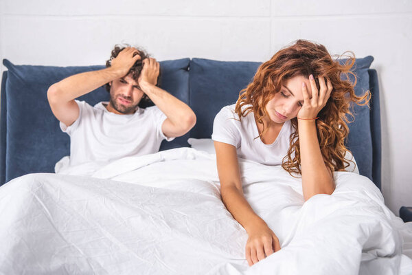 молодая пара сидит на кровати и страдает от головной боли по утрам
