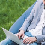 Asiático freelancer trabajando en portátil mientras sentado en frijol bolsa silla en césped