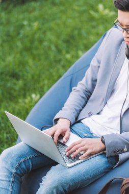 Asya freelancer fasulye çanta çim sandalyede otururken dizüstü bilgisayarda çalışma