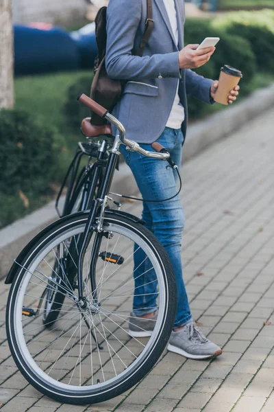 Обрезанный Вид Человека Кофе Идти Помощью Смартфона Опираясь Велосипед — Бесплатное стоковое фото