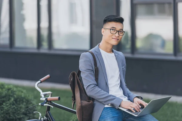 Smiling Asian Teleworker Using Laptop While Sitting Bicycle — Stock Photo, Image