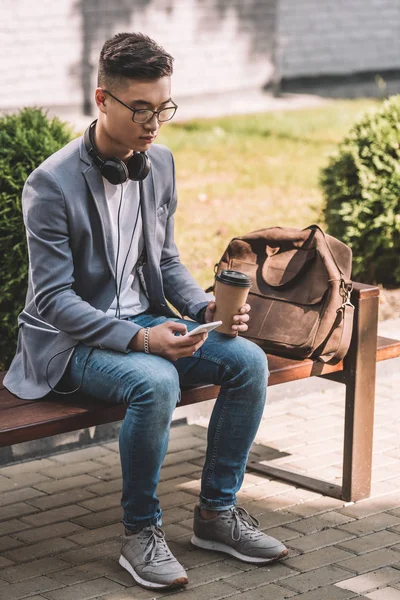 Asijský Krasavec Kávou Jít Smartphone Sluchátka Sedí Lavičce Kožený Batoh — Stock fotografie zdarma