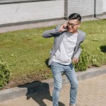 Asiatique homme avec ordinateur portable avoir conversation tout en équitation longboard sur rue