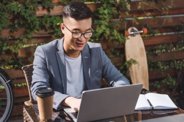Asya iş adamı uzak çalışma üstünde laptop kafede gülümseyen