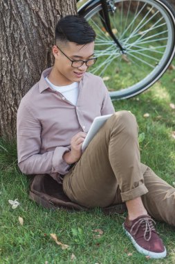 Asya adam sırt Park'ta dinlenme sırasında dijital tablet kullanma