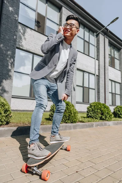 Стильный Азиатский Мужчина Ноутбуком Разговаривает Скейтборде Смартфоне — стоковое фото