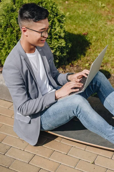 Asian Teleworker Using Laptop While Sitting Longboard Street — Free Stock Photo