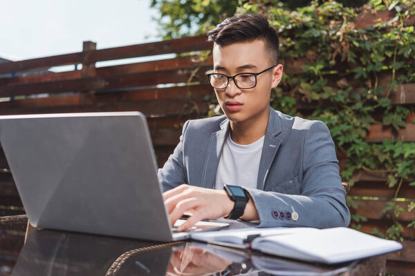 азиатский бизнесмен удаленно работает на ноутбуке в кафе
