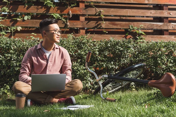 Asiático Hombre Con Portátil Mirando Lejos Mientras Remoto Trabajo Portátil — Foto de stock gratis